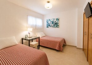 Una habitación con dos camas, una mesita con una lámpara, un cuadro y un televisor sobre un mueble de madera.