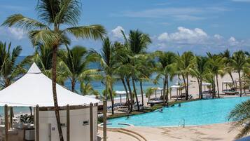A pool area with palm trees, lounge chairs, and a beach view.