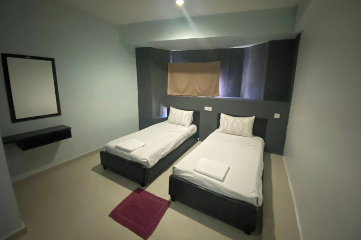 Une petite chambre d’hôtel moderne, avec deux lits simples, un miroir et un tapis rouge.