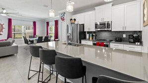 A modern kitchen with white cabinets, stainless steel appliances, and a central island with bar stools. - Family-friendly escape w/ resort access & pool (Kissimmee)