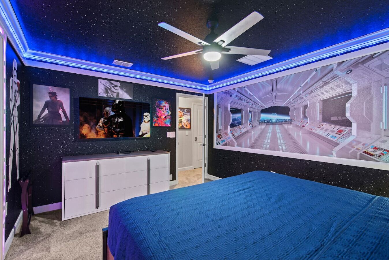 A bedroom with a starry ceiling, a bed, a vanity, and a wall mural of a spaceship interior.