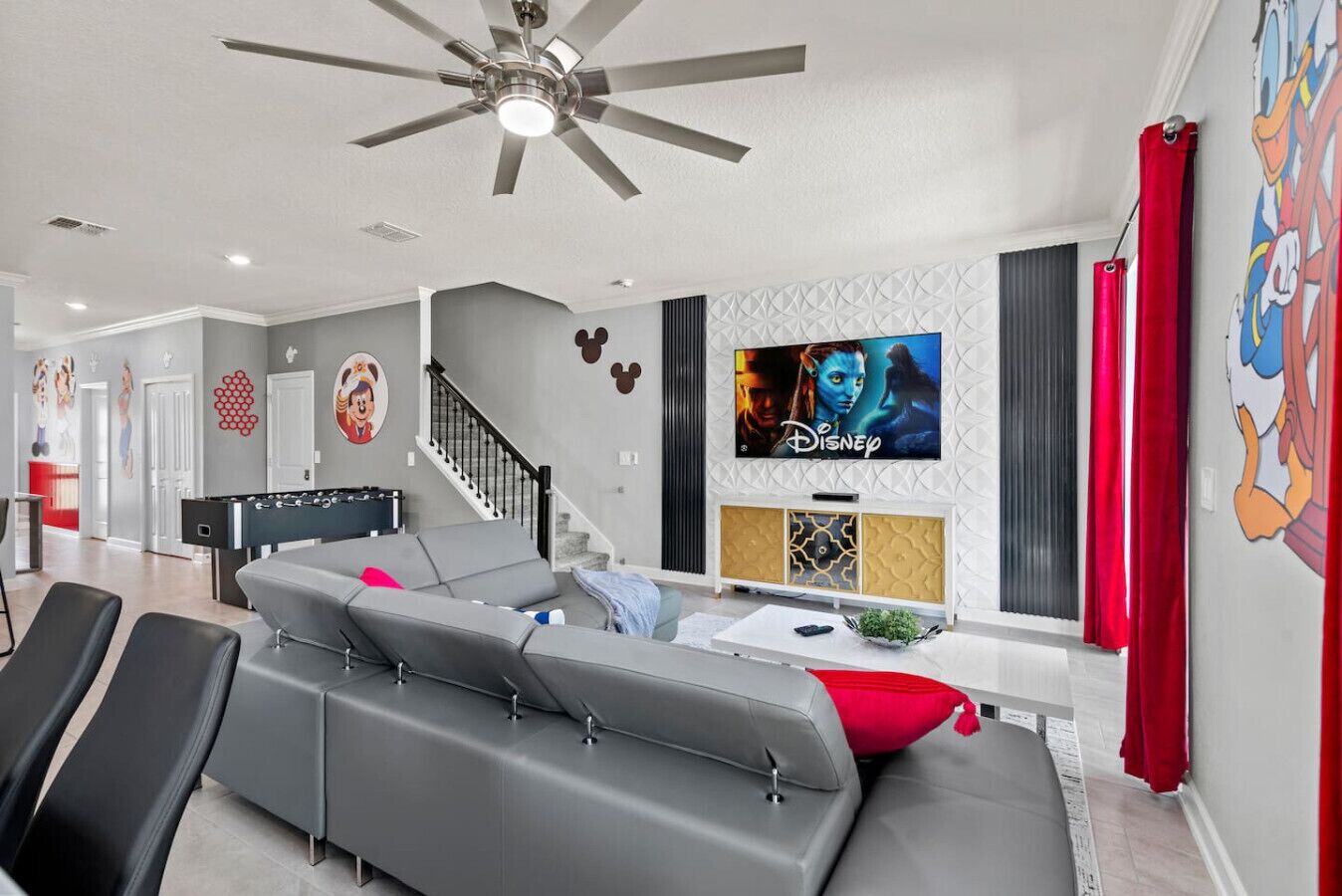 A modern living room with a grey sectional sofa, a flat-screen TV mounted on the wall, and a ceiling fan.