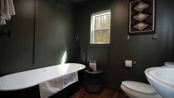 A bathroom with a freestanding bathtub, a toilet, and a window.
