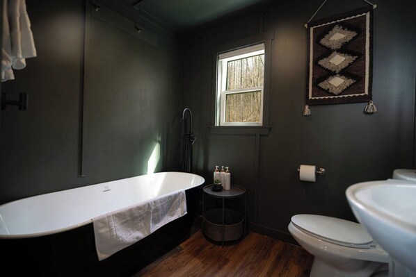 A bathroom with a freestanding bathtub, a toilet, and a window.