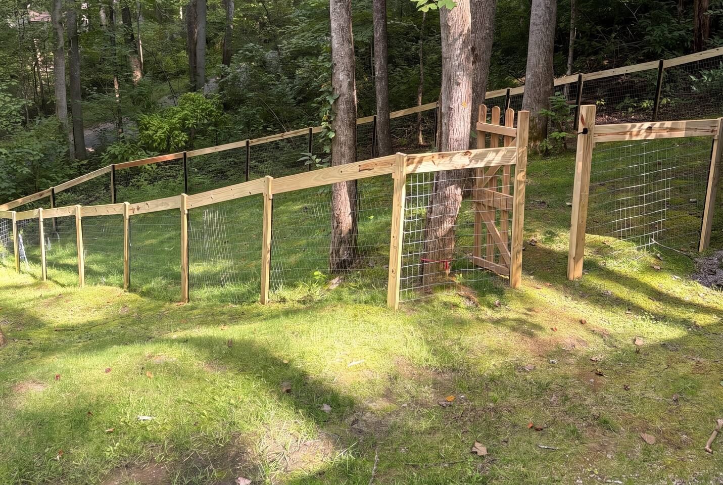 Un espacio al aire libre cercado con una estructura de madera, rodeado de árboles y césped.
