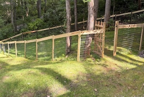 A fenced outdoor area with a wooden structure, surrounded by trees and grass.