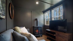 Ein gemütliches Wohnzimmer mit einer Couch, einem Fernseher, einem Kaminofen und großen Fenstern.
