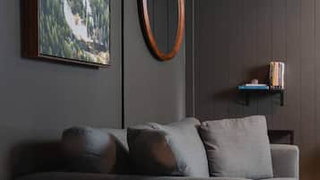 Una sala moderna con un sofá gris, un cuadro de un paisaje, un adorno circular de madera y una pequeña estantería.