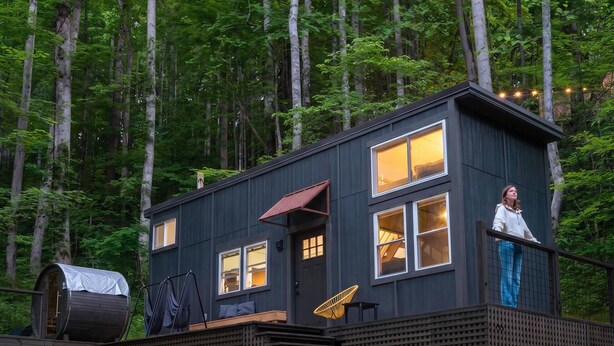 Eine Holzhütte mit einer Terrasse, einem überdachten Bereich und einem Fenster mit Blick auf einen Wald.