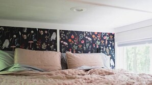 Ein Bett mit einer rosa Decke, einem blumigen Kopfteil und einem Fenster mit Blick auf Bäume.