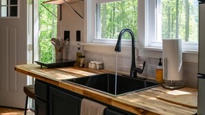 Eine Küche mit einer Holzausziehtafel, einem schwarzen Spülbecken und einem Fenster mit Blick auf Bäume.