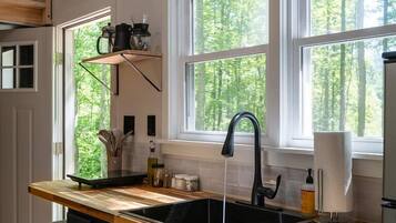 Una cocina con encimera de madera, un lavamanos negro y una ventana con vistas a árboles.
