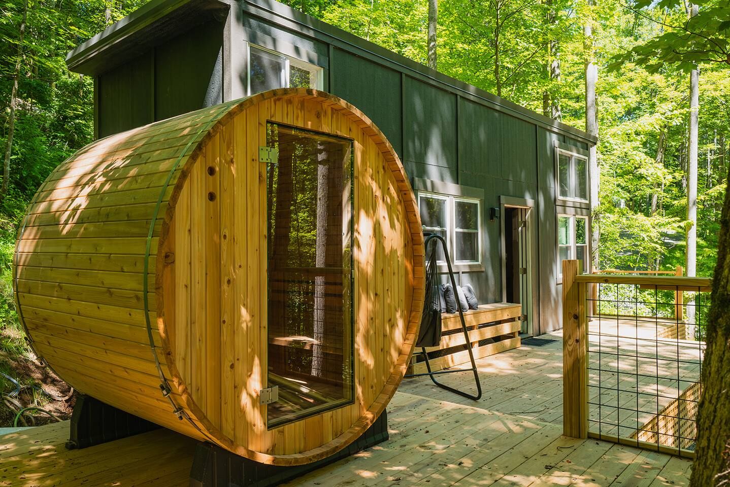 Una cabana amb una gran estructura de fusta en forma de barril, una terrassa i una zona tancada per una tanca.
