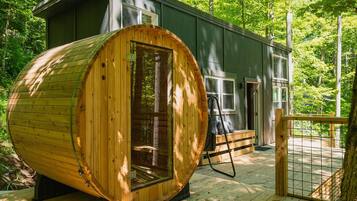 Una cabana amb una gran estructura de fusta en forma de barril, una terrassa i una zona tancada per una tanca.