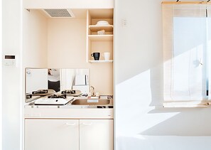 Una cocina moderna con estufa, lavamanos y armarios. Se aprecia una ventana con persianas a la derecha.