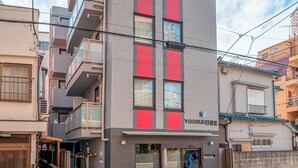 Un edificio de varios pisos con un diseño moderno, que combina paneles grises y rojos, y una fachada comercial con señalización.