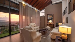 A spacious living room with a large window, a sofa set, a coffee table, and a lamp. - Swarga Villa (Kandy)
