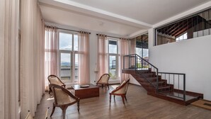 A spacious living area with wooden flooring, a staircase, and large windows with curtains. - Swarga Villa (Kandy)