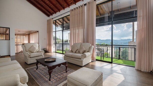 A spacious living room with two beige sofas, a wooden coffee table, and a large window with a view of a green landscape. - Swarga Villa (Kandy)