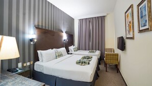 A hotel room with two beds, a desk with a lamp, a chair, and a TV on the wall. - Cube Hotel Dubai (Dubai)