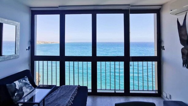 A room with a large sliding glass door leading to a balcony with a view of the sea.