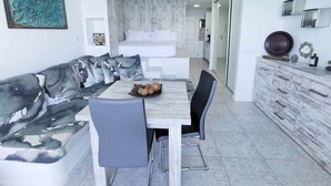 A modern dining area with a wooden table and chairs, a sofa with a patterned cover, and a white cabinet with drawers.