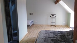 A room with a sloped ceiling, a bed, a hanging light fixture, and a clothes rack. - Gîte mon p'ti bout (LES ROCHES L'EVËQUE)