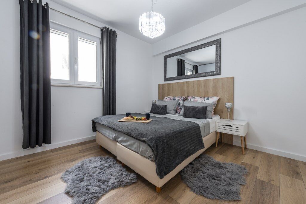 A modern bedroom with a wooden headboard, a large mirror, a bedside table, and a fluffy rug.