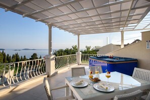 Een balkon met uitzicht op zee, een jacuzzi en een tafel gedekt voor twee met borden en drankjes.