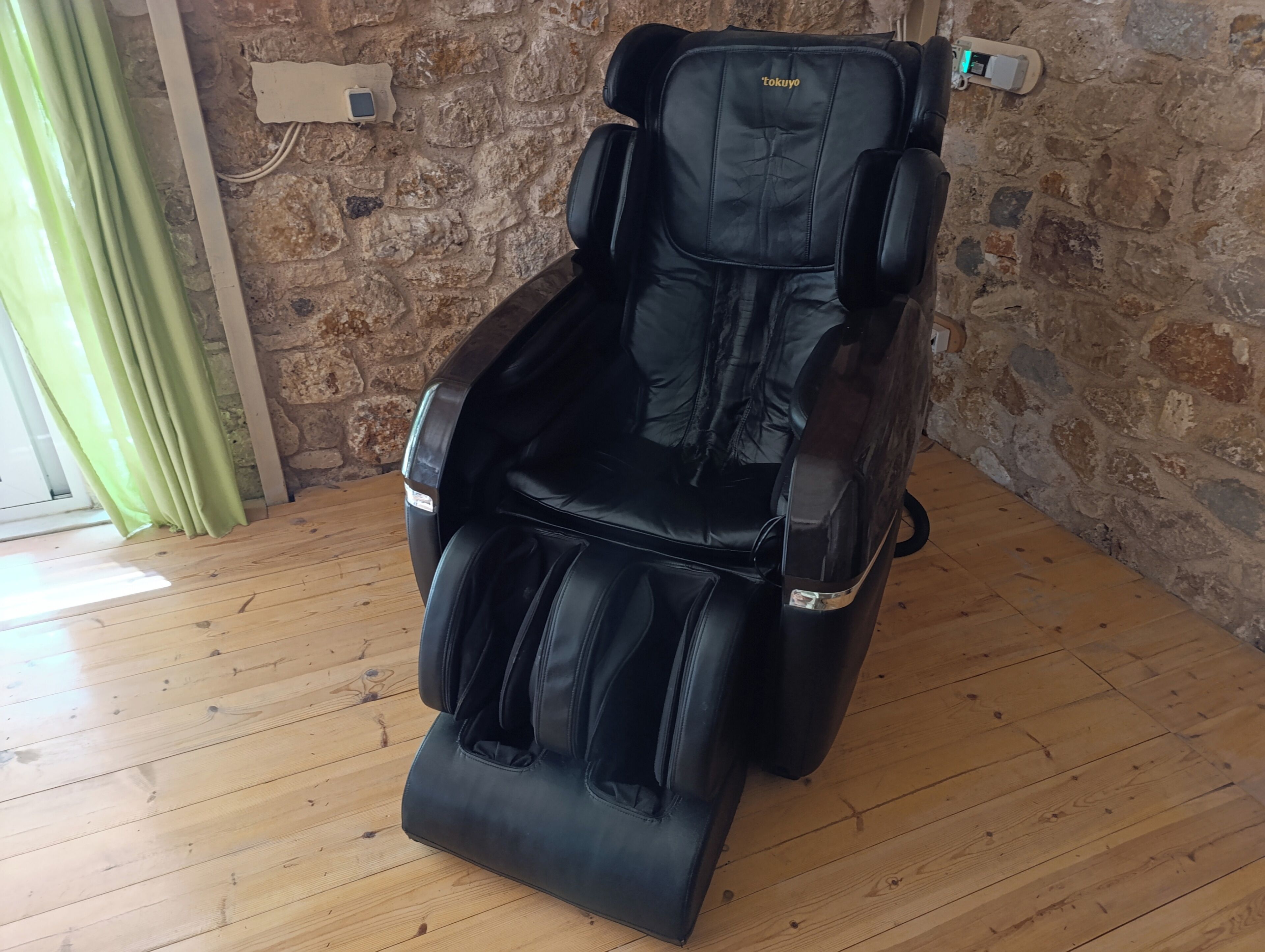 A massage chair in a room with a stone wall and wooden flooring.