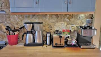 Una cocina con pared de piedra, una cafetera, un tostador y diversos utensilios de cocina.