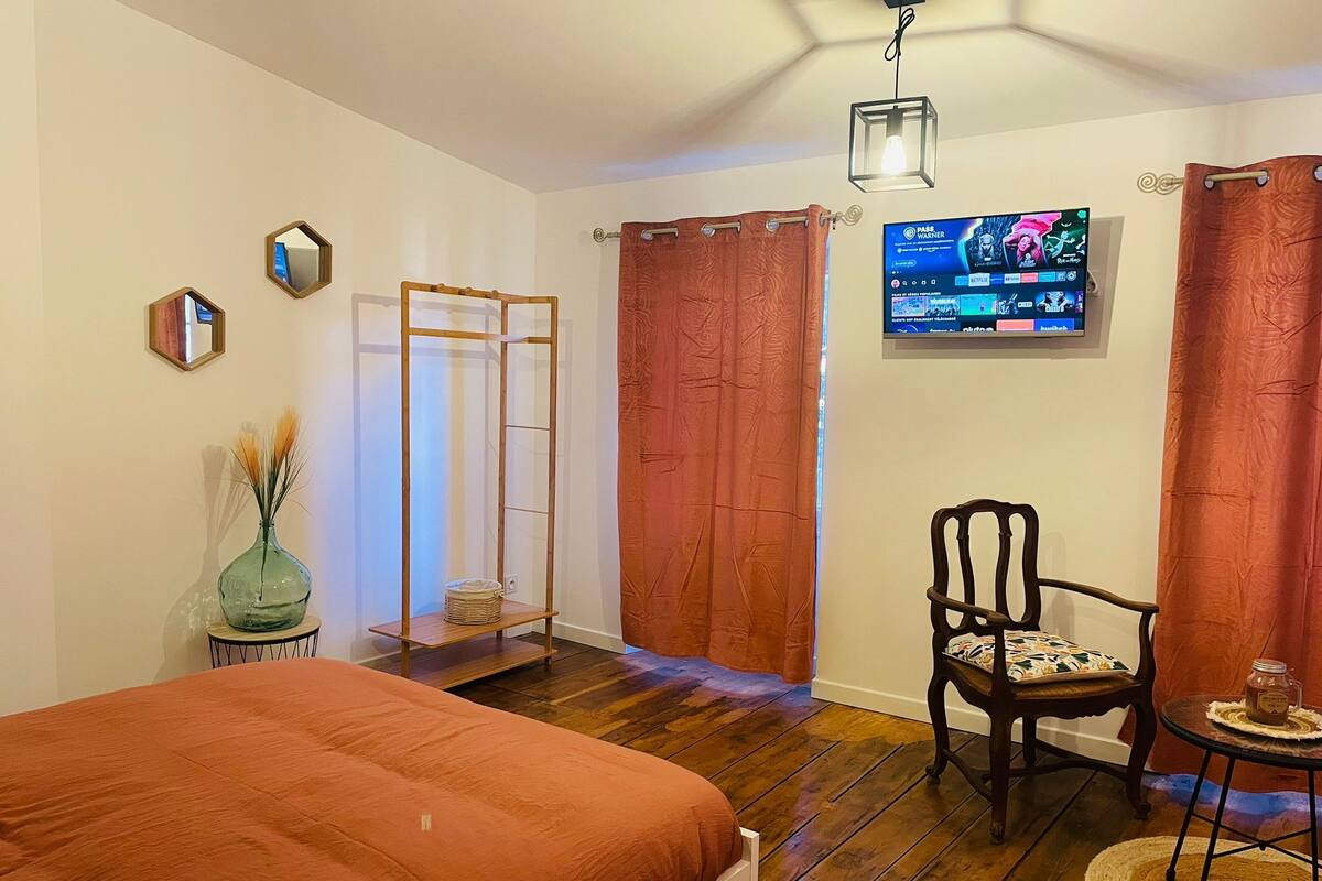 A bedroom with a bed, a chair, a small table, a TV, and a wardrobe.