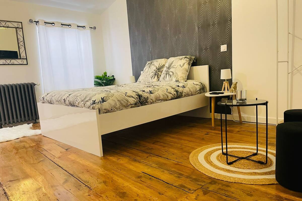 A modern bedroom with a bed, bedside table, lamp, and a small plant.