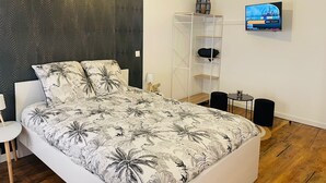 A modern bedroom with a bed, a TV, a white shelving unit, and a small table.