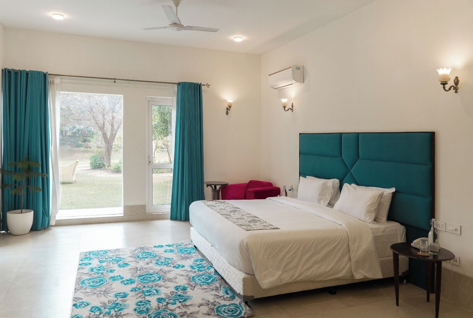 A bedroom with a bed, a nightstand, a potted plant, a window with curtains, and an air conditioning unit.
