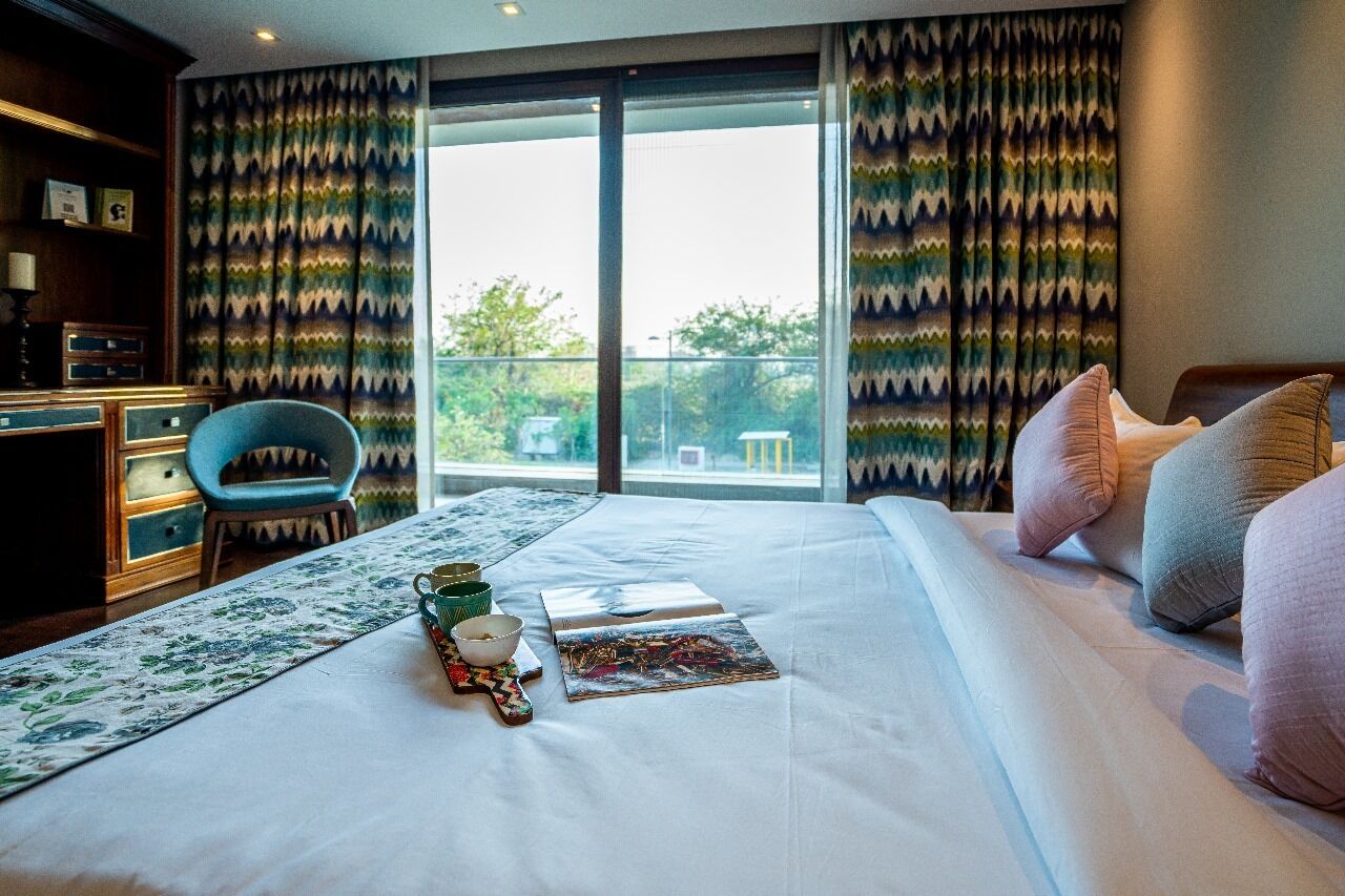 Habitación de hotel con cama, escritorio, silla y vistas amplias por un ventanal.