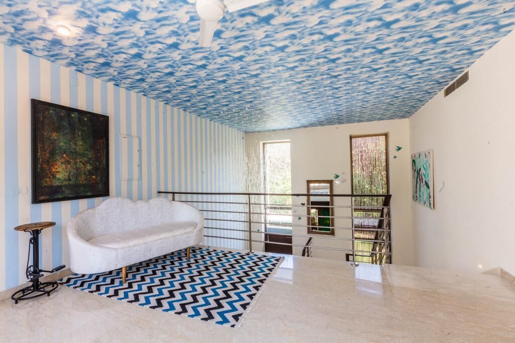 Una habitación con una bañera blanca, paredes a rayas, un techo con estampado de nubes, una alfombra blanco y negro y una barandilla de metal.
