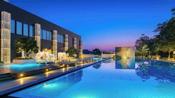 Un hotel moderno con una amplia piscina exterior, sillones de descanso y una fachada bien iluminada.