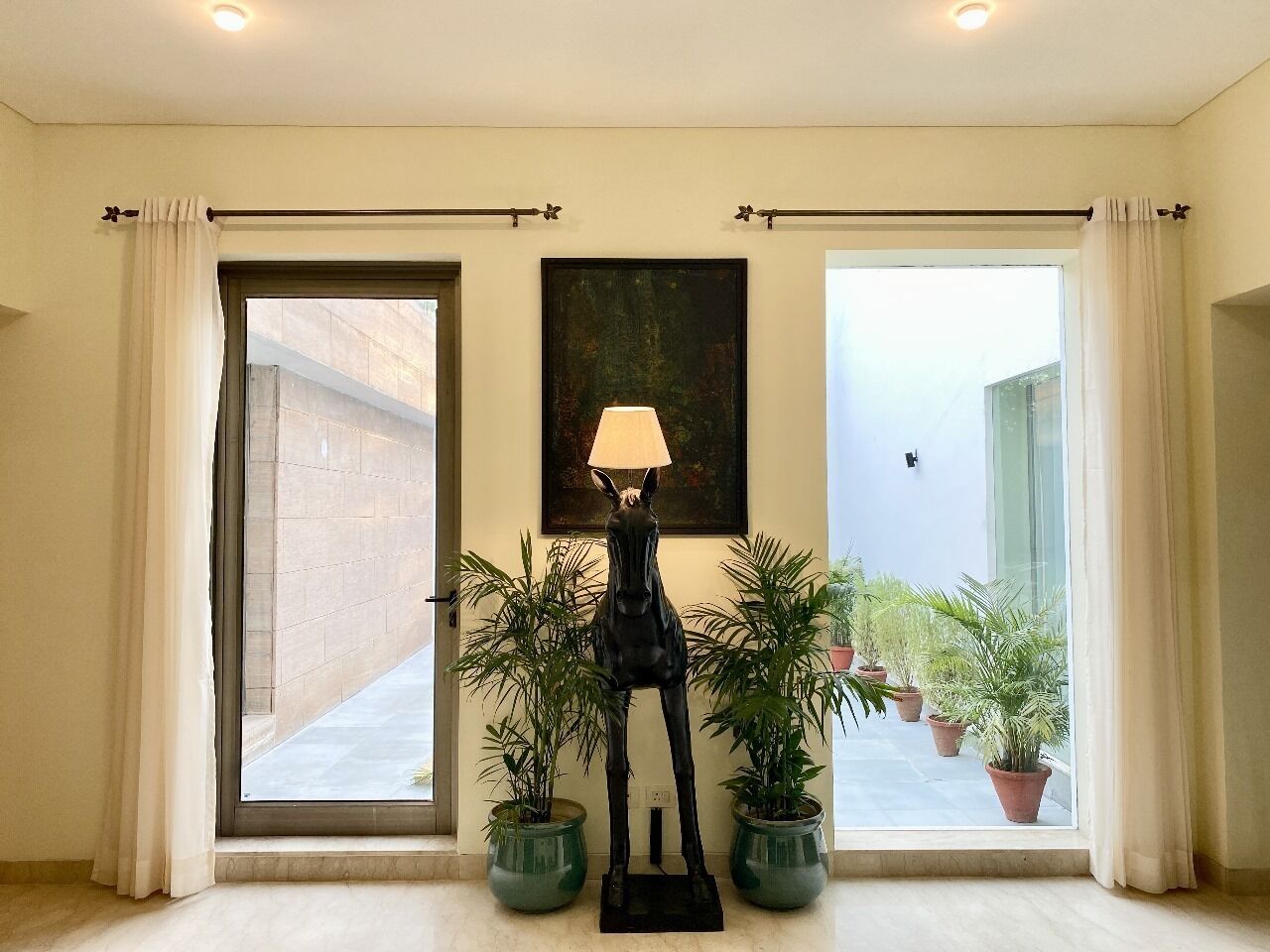 A room with a large window, a lamp, and potted plants.