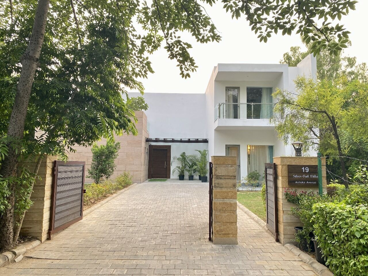 A gated entrance to a modern villa with a paved driveway, a gated driveway, and a sign indicating the property name and address.