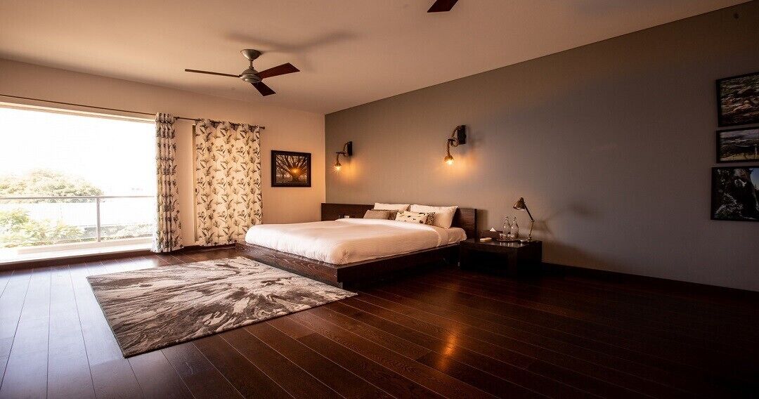 A bedroom with a large bed, a ceiling fan, a nightstand with a lamp, and a window with curtains.