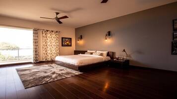 A bedroom with a large bed, a ceiling fan, a nightstand with a lamp, and a window with curtains.