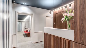 A modern hallway with a reception desk, a wooden panel wall, and a door leading to a room with a red bench and a vase of flowers. - Sospeso Boutique Hotel (Milan)