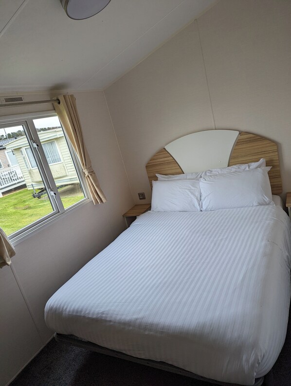 A neatly made bed with white linens in a hotel room. - Cayton Caravan Holidays (Scarborough)