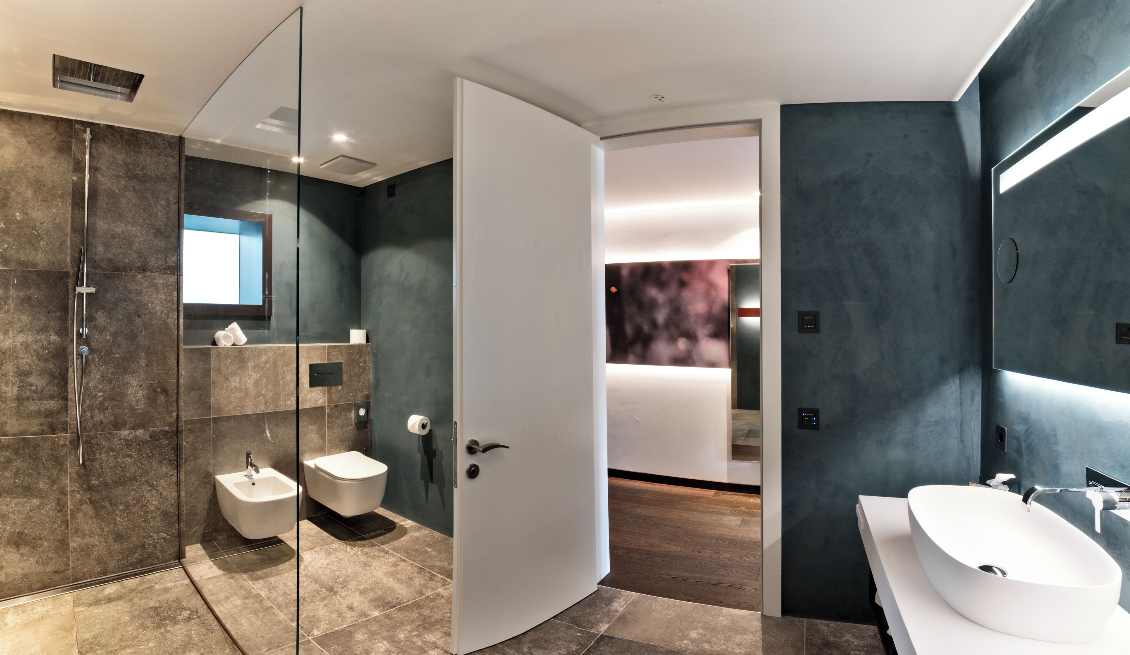 A modern bathroom with a glass shower enclosure, a bidet, a toilet, and a large white sink.