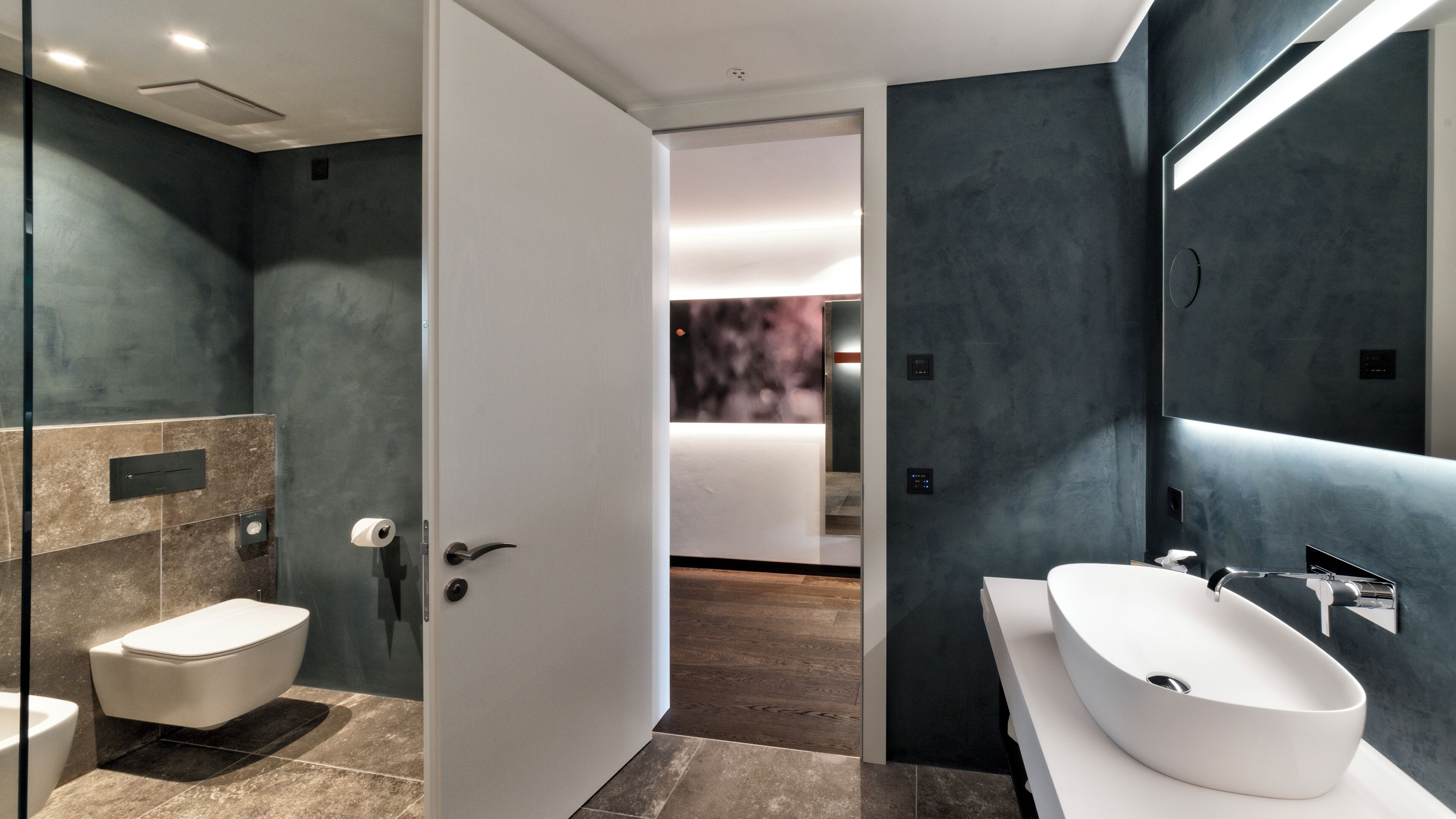 A modern bathroom with a large white sink, a glass shower enclosure, and a marble-tiled floor.