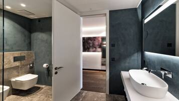 A modern bathroom with a large white sink, a glass shower enclosure, and a marble-tiled floor.