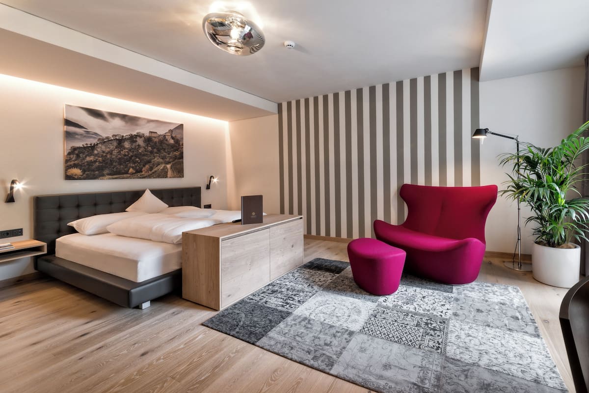 A modern bedroom with a bed, a red chair, a desk, and a potted plant.