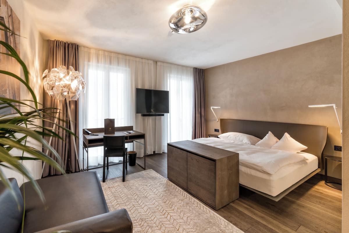 A hotel room with a bed, desk, chair, television, and a large plant.
