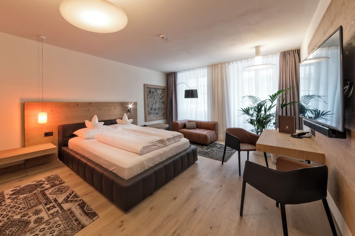 A modern hotel room with a large bed, a desk, a chair, a TV, and a plant.